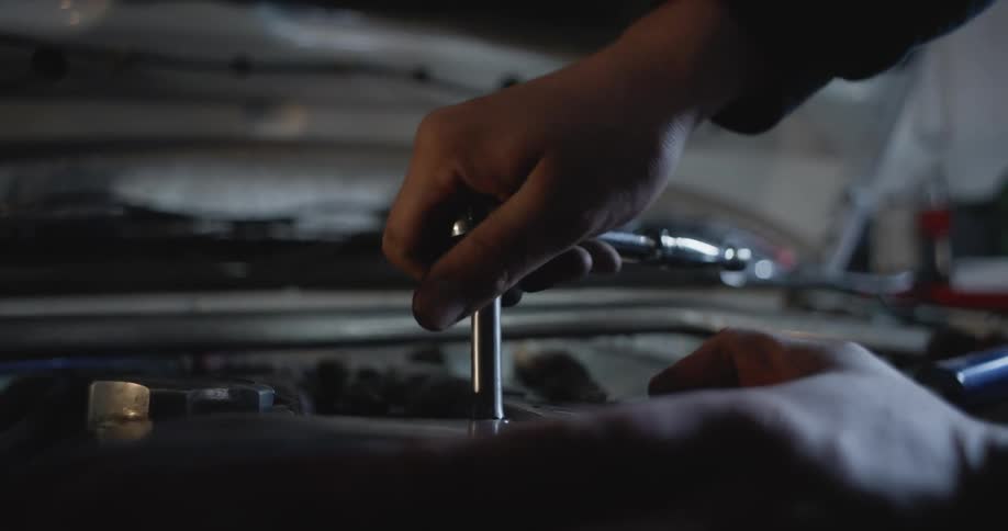 A mechanic uses a socket wrench while working under the hood of a car