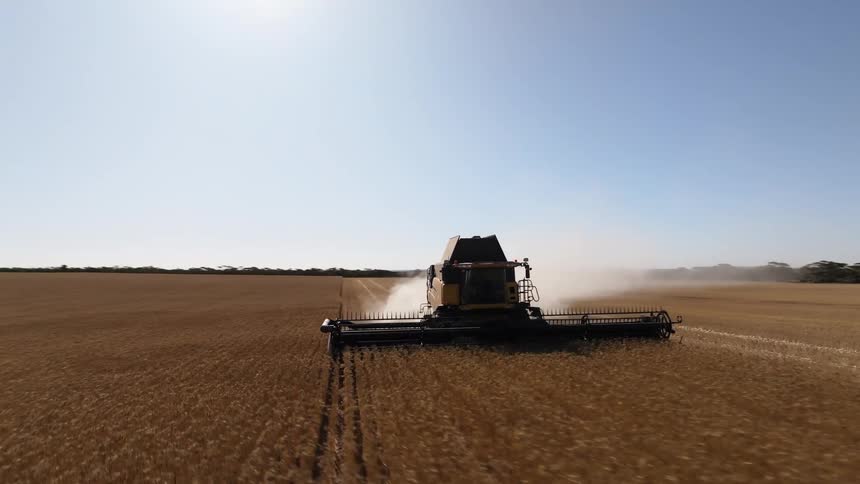 A tractor plows through a field with a trail of dust behind it on a sunny day under blue skies