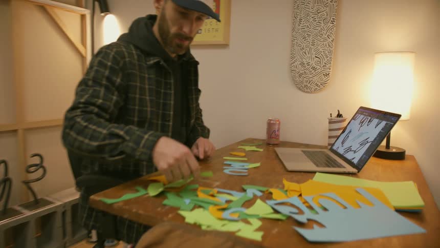 Man sitting at a desk on a small office selecting pieces of cut colorful cardboard