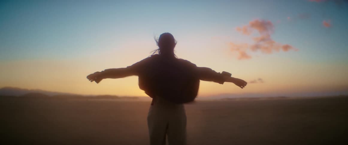 Silhouette of a woman standing with her arms wide open in in the desert at evening