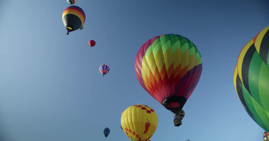 The sun shines on colorful hot air balloons as they float in a clear blue sky