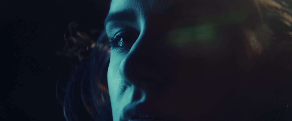 Colored light flashes onto womans face as she stands next to digital screen