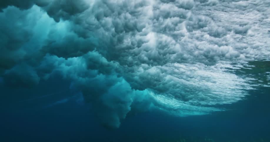 Underwater view of waves rolling overhead and sunlight reflecting the ripples and sparkles as water splashes