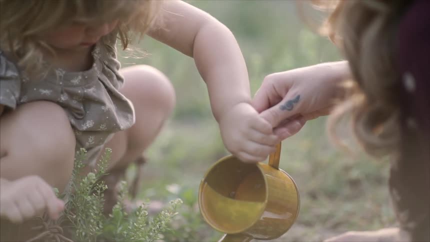 A child takes a pot from a woman and begins watering the soil