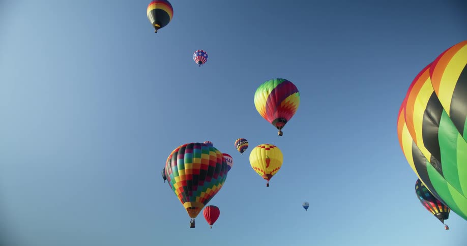 The sun shines on colorful hot air balloons as they float in a clear blue sky