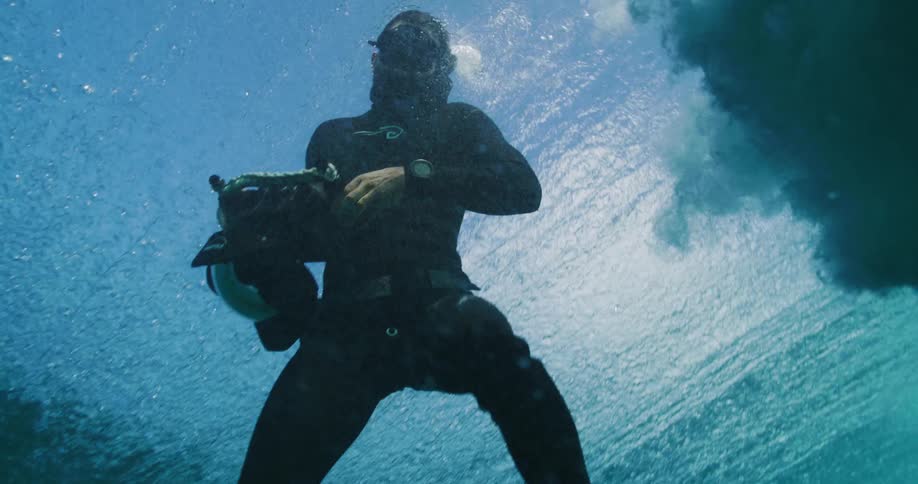 Scuba diver holding a camera underwater gets carried away by the waves