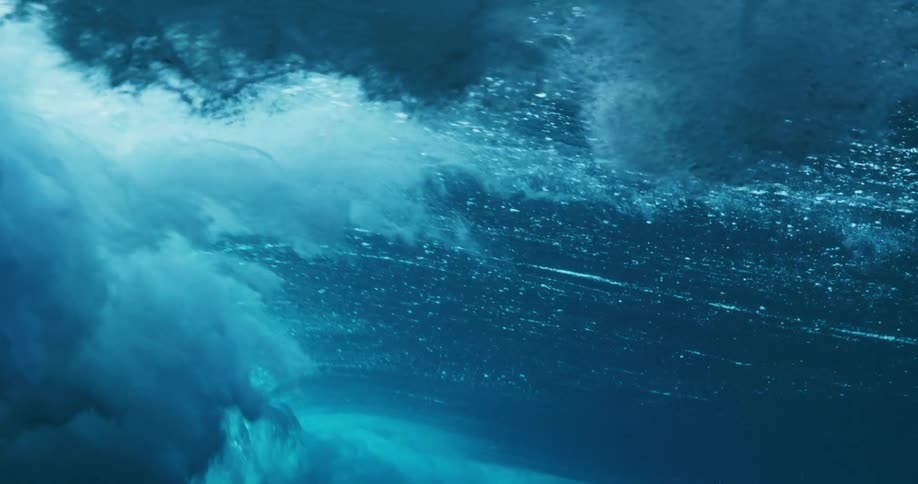 Underwater view of waves rolling overhead and sunlight reflecting the ripples and sparkles as water splashes