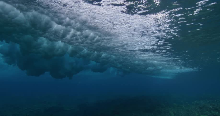 A wave rolls over the surface of the ocean causing the sea floor below to become shrouded in darkness