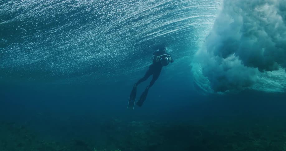 Diver floats near surface as wave rolls and crashes over seafloor