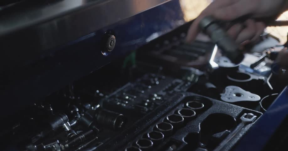 A man is reaching into his toolbox and taking a socket wrench
