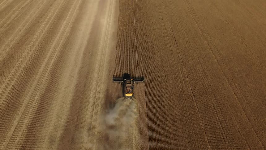 A tractor is plowing a field on a farm and leaving behind a cloud of smoke