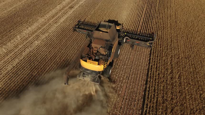 A tractor is plowing a field on a farm and leaving behind a cloud of smoke