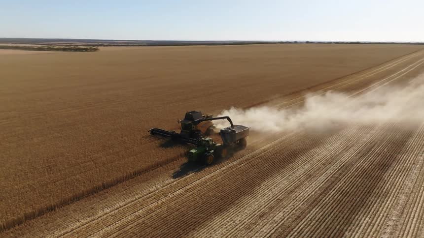 Tractors on a farm are plowing a field and leaving a trail of smoke
