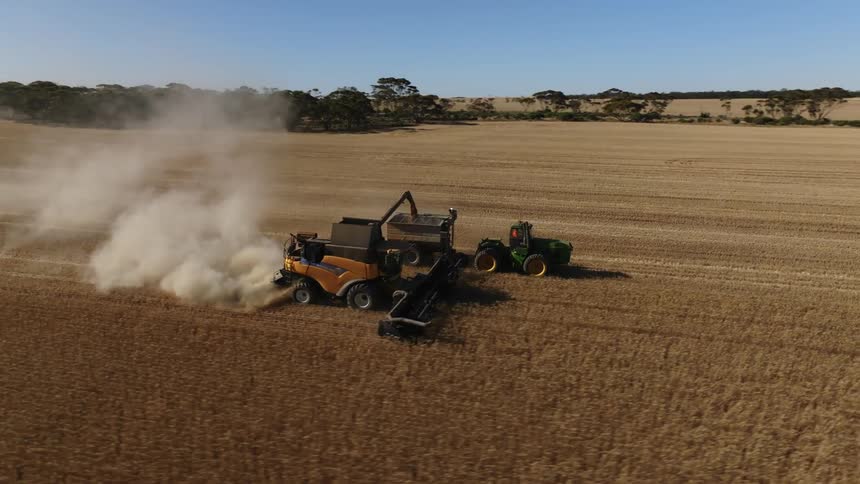 Tractors on a farm are plowing a field as smoke emerges from one of the plows