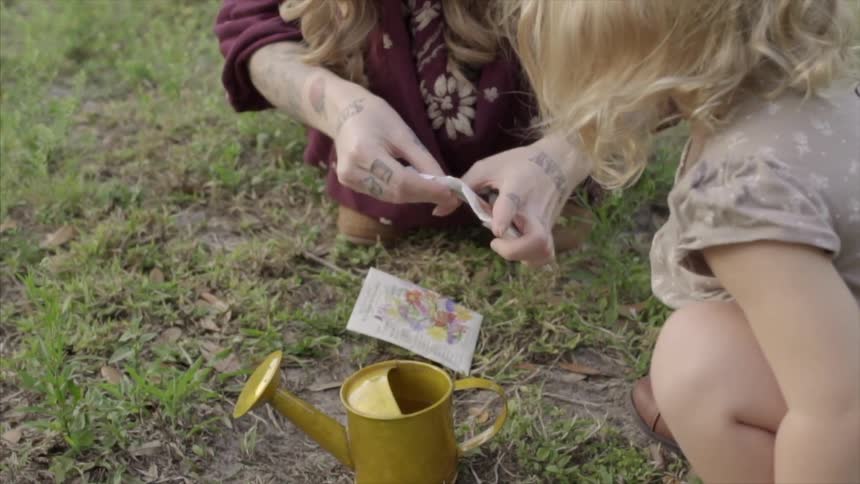 A woman opens a seed packet as a small girl watches