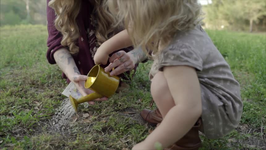 A woman and small girl using a watering can to water newly planted seeds