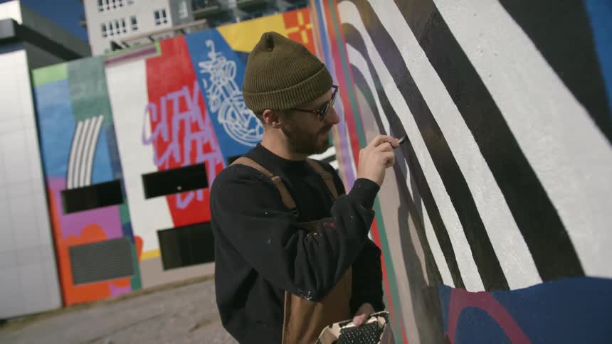 Hipster artist painting a mural on outdoor wall of building