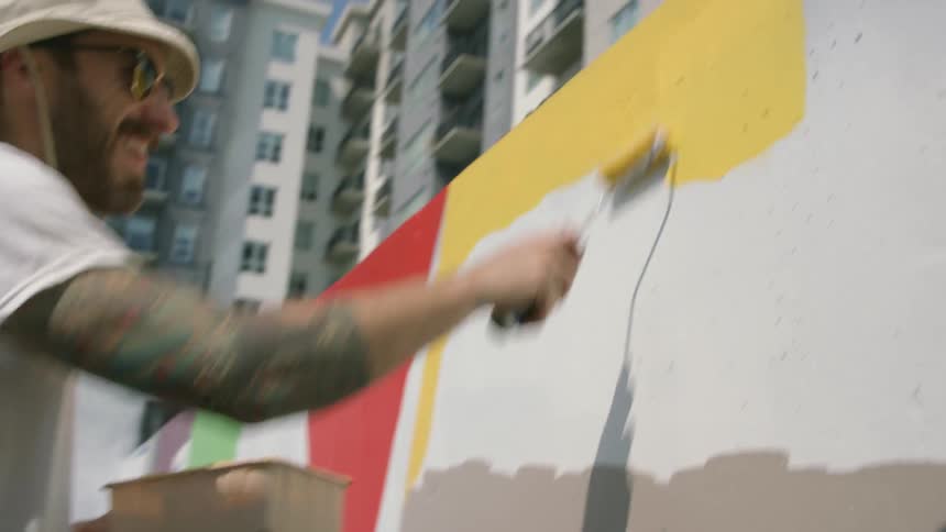 A man is standing outside painting a design on the wall of a building