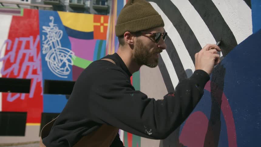 A man is standing outside painting a design on the wall of a building