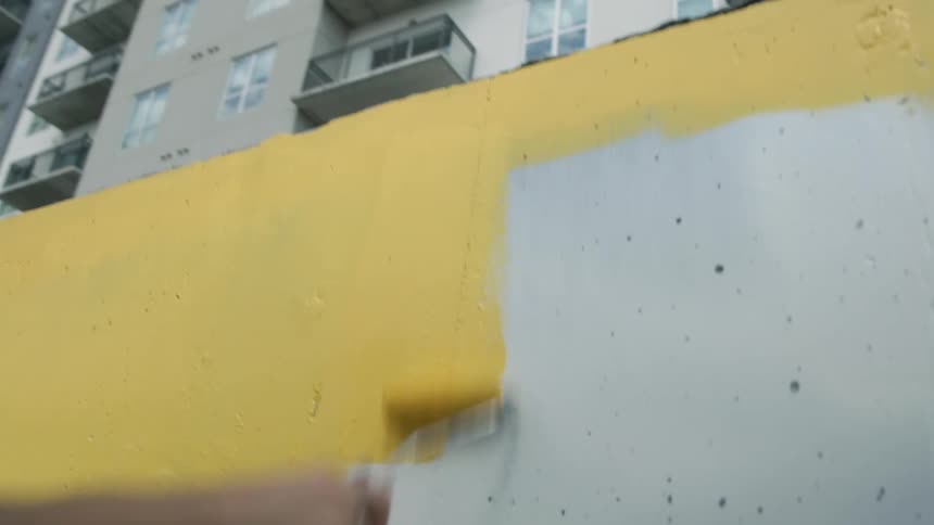 A man is standing outside painting a design on the wall of a building