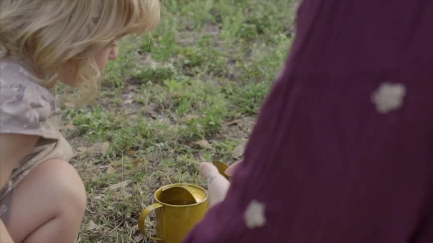 A woman and girl crouch before a watering pot