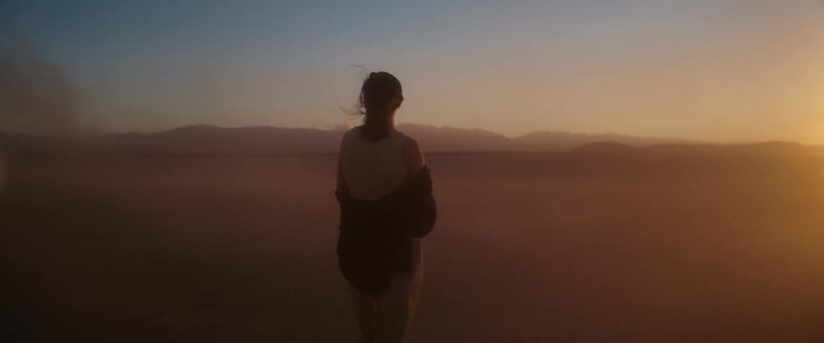 Woman walks towards the sun setting over mountains in the desert