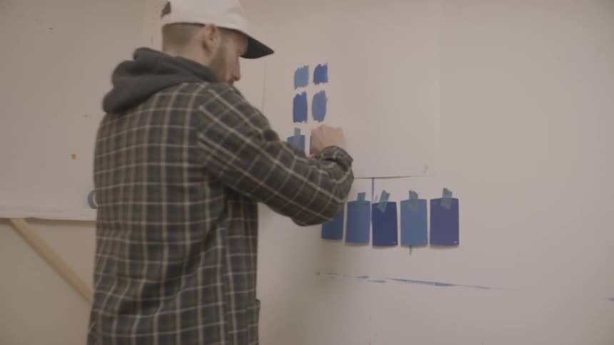 Male taping swatches of blue paint color on white wall