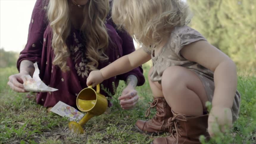 A woman helps a little girl water newly planted seeds