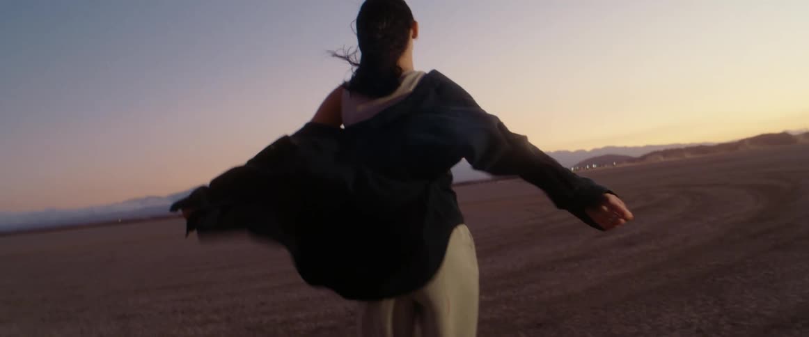 Young woman stands on the desert while the wind blows at evening