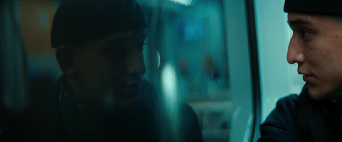 A young man is sitting on a train looking out the window as it travels at night