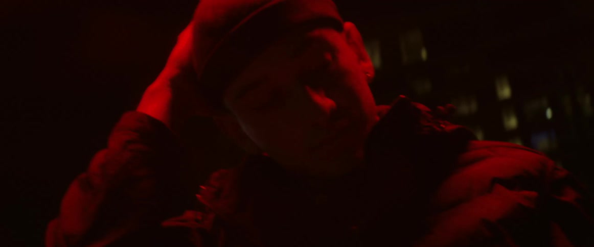 A man is outside at night under a red light and holding his head in dismay