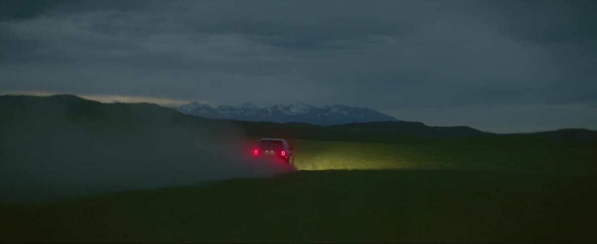 Car driving on the green plains with headlights on at evening