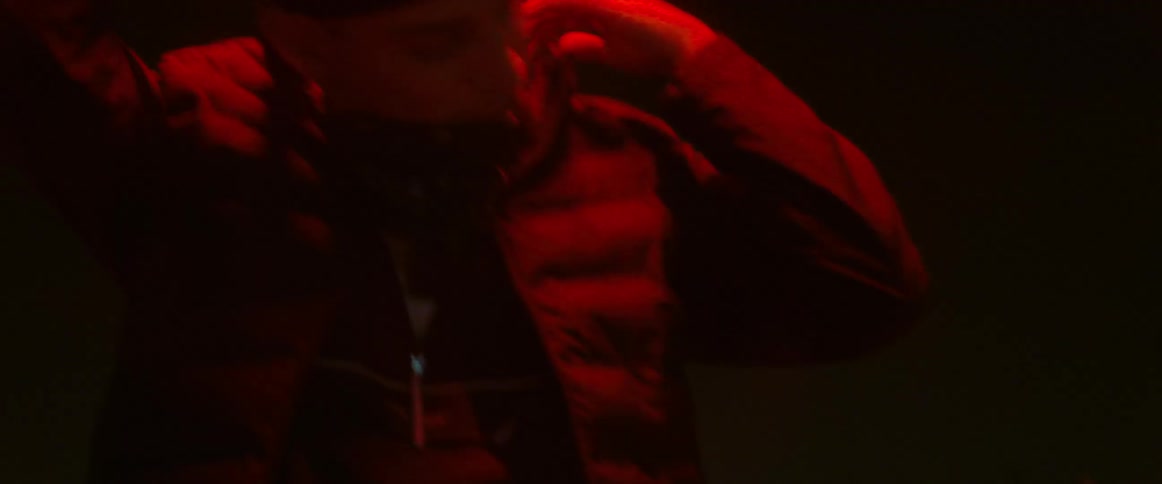 Man runs his hand down his neck and chest while performing under red colored lighting