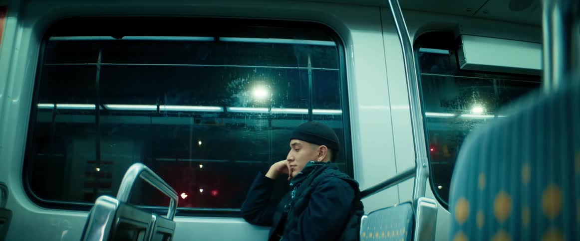 A man rests his head against his hand while riding a bus at night