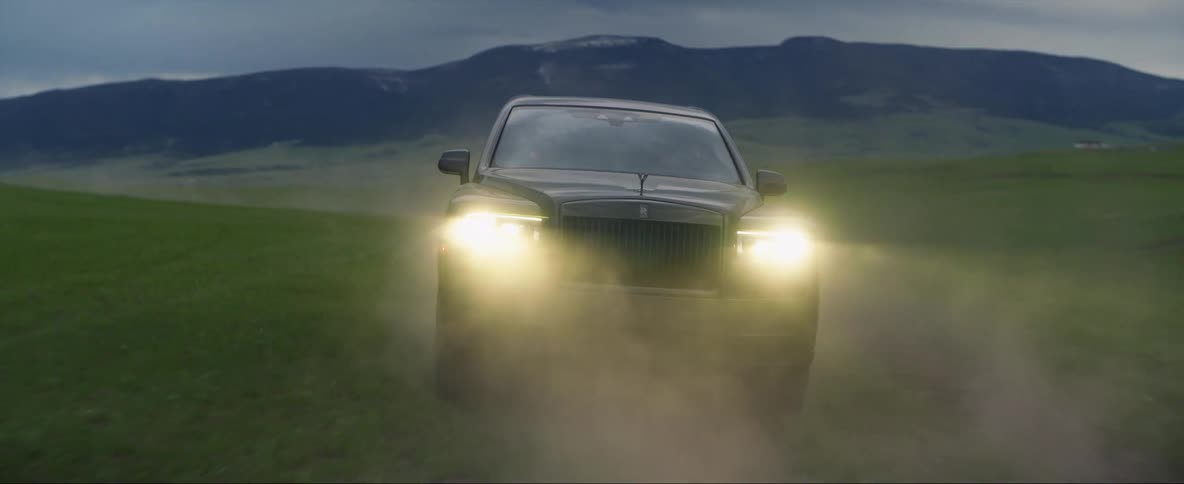 Car driving rapidly on a road across a field in the country at dusk