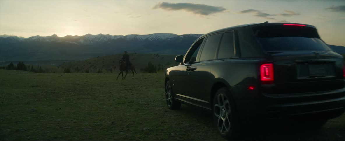 Sunlight shines above mountains on horizon as horse riders stop to greet arriving vehicle