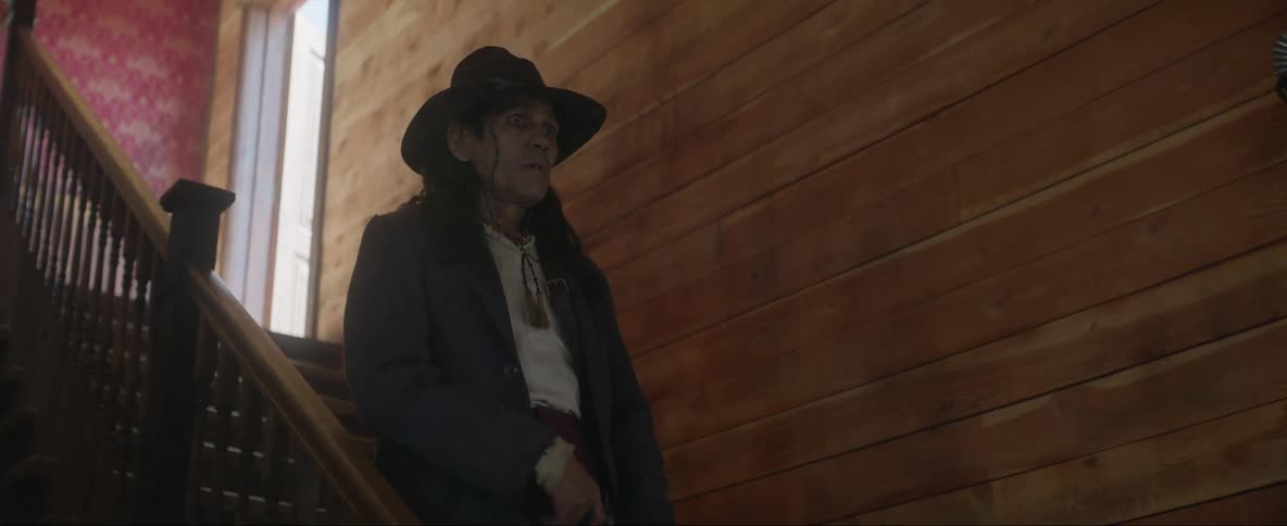 A man in a hat walks down the stairs of a saloon draws his gun is hot and tumbles down the stairs
