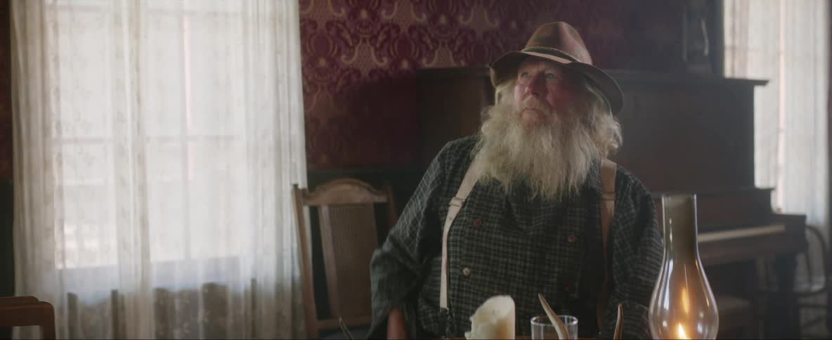 A man is sitting down having a drink and he looks up and sets his drink on the table as he reaches for his gun and then falls to the ground