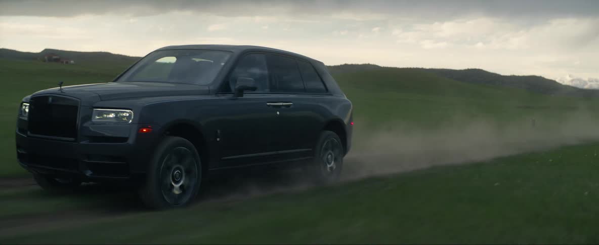 A black truck travels on a rural road with mountains in the distance under a cloudy sky