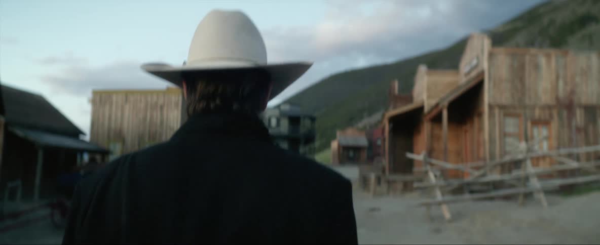 An outlaw wearing a white cowboy hat walking through a western town in the wild west