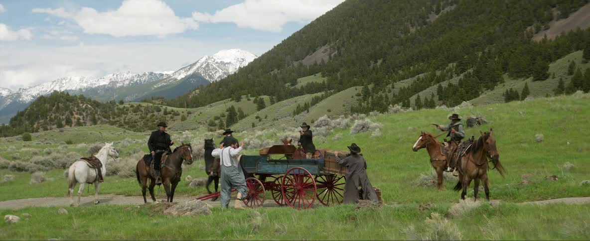 A group of outlaw cowboys ambush a man driving a wagon on a solitary road in the mountains