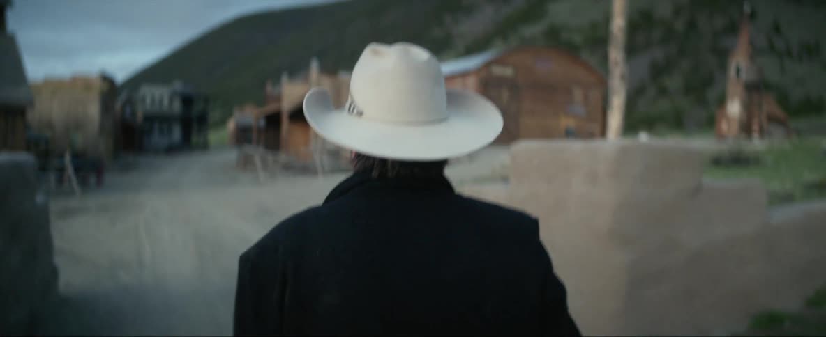 A man wearing a cowboy hat is walking around an old west town