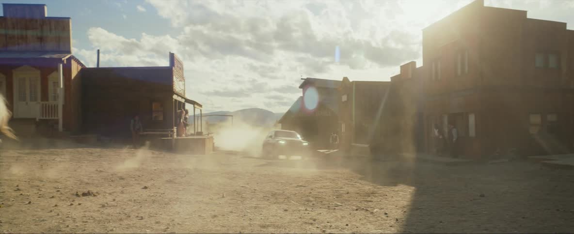 A woman in a small rural town points a gun at men on horses who then gallop away as a vehicle speeds in to town and chases them