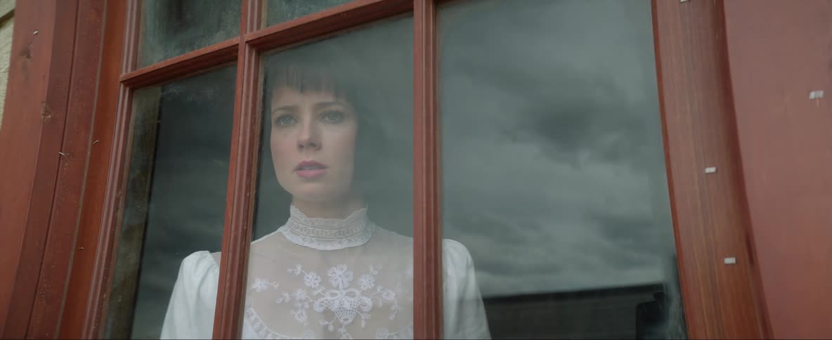 Woman wearing an old time dress looks out the window in anger
