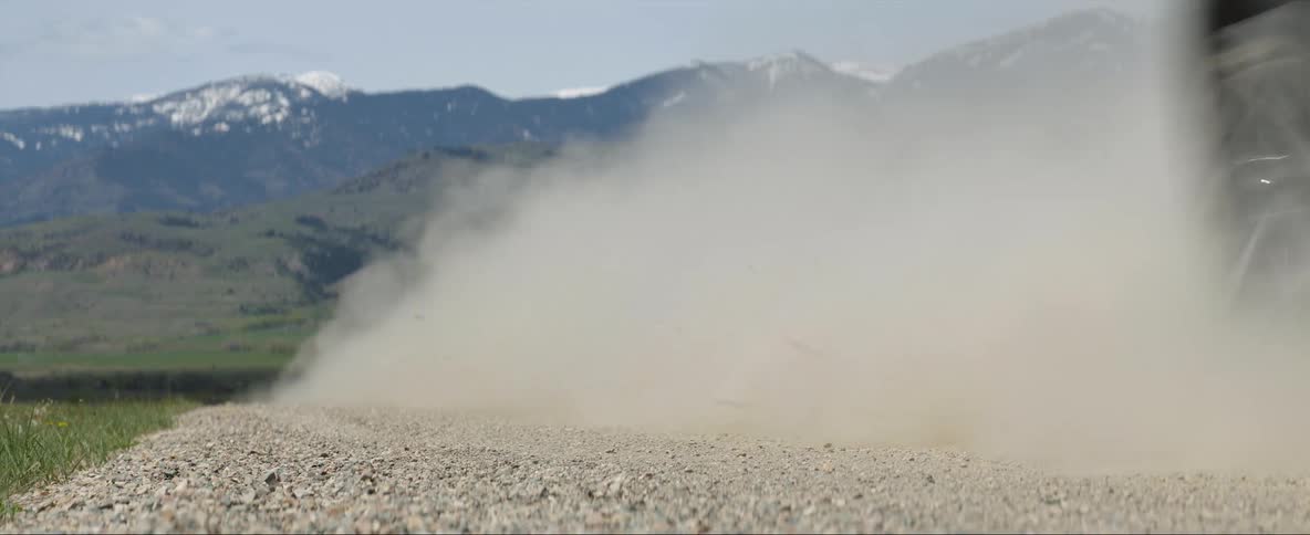 Black vehicle drives full speed on a dirt road next to the mountains
