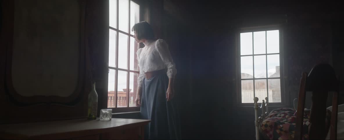 A woman is tying her shoelace then looks out the window and walks out of the room