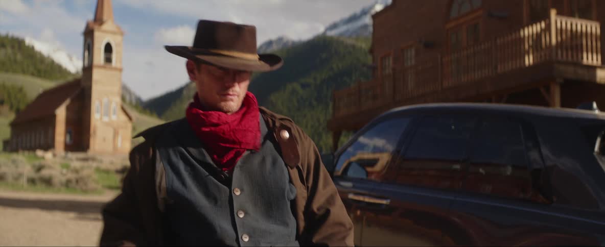 A cowboy is walking out of his vehicle in a rural area