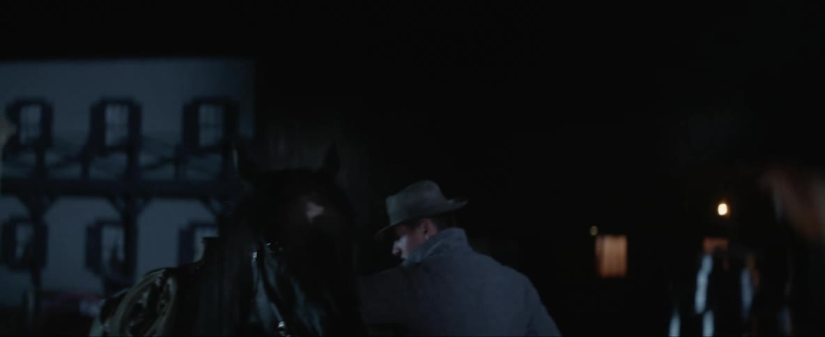 Woman stands outdoors at night in old western town holding lantern while saying goodbye to departing horseman