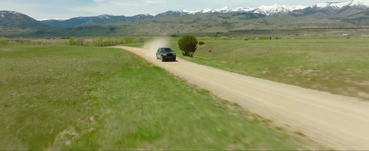 Car driving rapidly on dirt road across a field in the countryside
