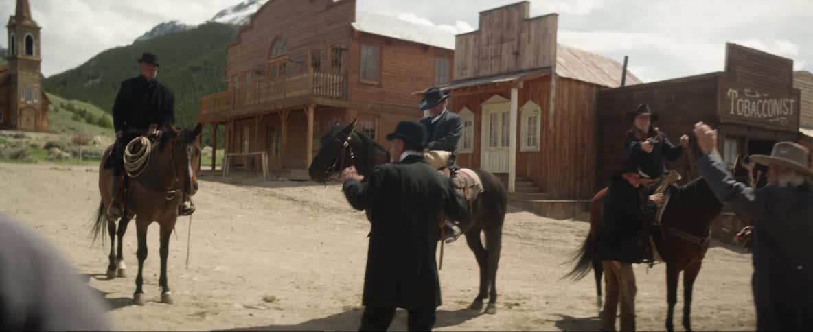 People working in a saloon confront cowboys on horses with a rifle